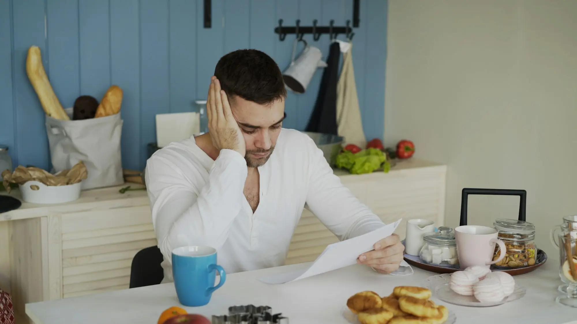 Business owner reading a letter at a kitchen table with a laptop and coffee nearby